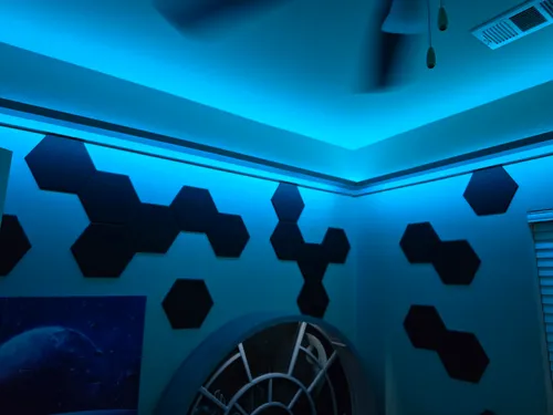 Hexagonal acoustic tiles on the wall near a glowing LED-lit ceiling corner
