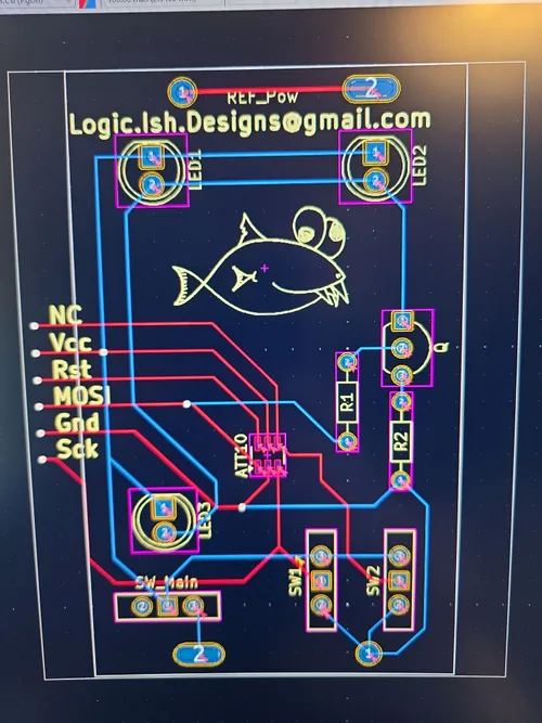 Custom PCB layout in design software showing the ATtiny10 footprint, LEDs, resistors, switches, and the Logicish fish mascot silkscreened on the board