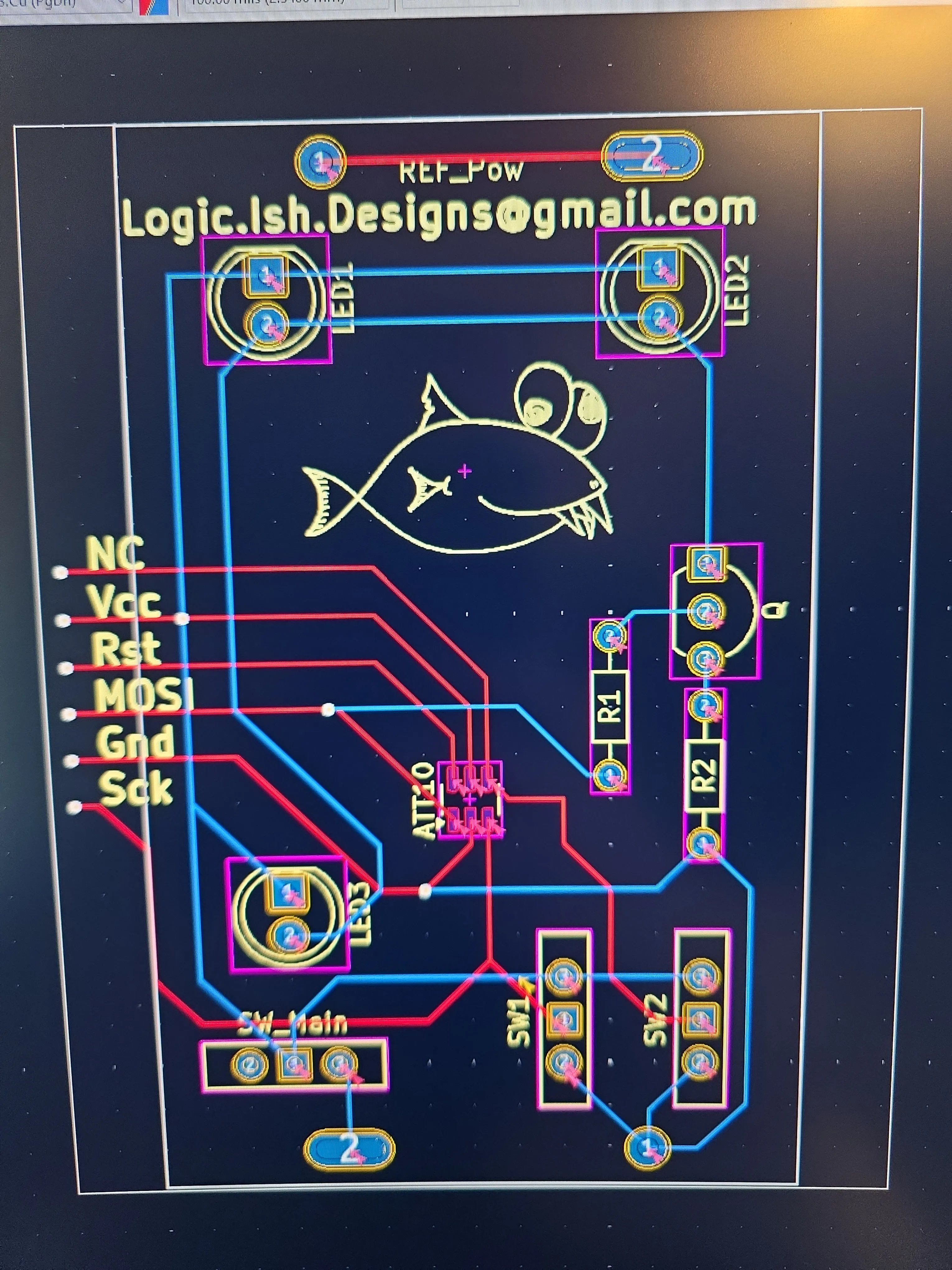 Custom PCB layout in design software showing the ATtiny10 footprint, LEDs, resistors, switches, and the Logicish fish mascot silkscreened on the board
